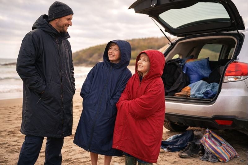 Parent and children standing by a car at a UK beach, wearing outdoor changing robes and staying warm after swimming
