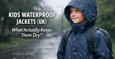 Primary school child wearing a navy waterproof jacket in steady UK rain, with raindrops beading on the fabric and blog title text overlay about choosing kids waterproof jackets.