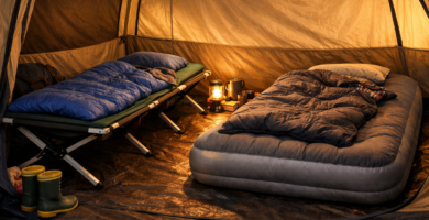 Camping bed with sleeping mat and air mattress set up side by side inside a family tent with warm lantern light
