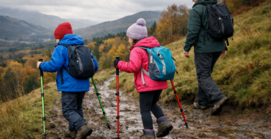 Parent and two children walking on a muddy hillside trail using adjustable hiking poles under an overcast sky on a UK family walk