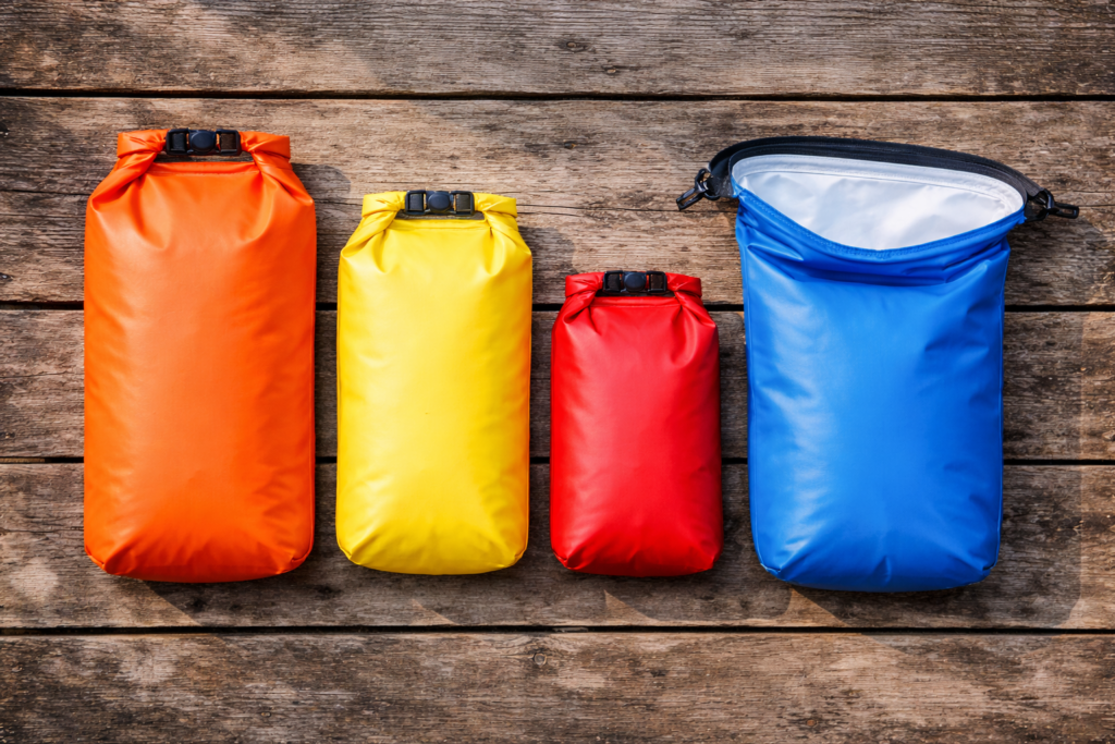 Four dry bags in different sizes and colours laid out for paddle boarding including one sealed and one open